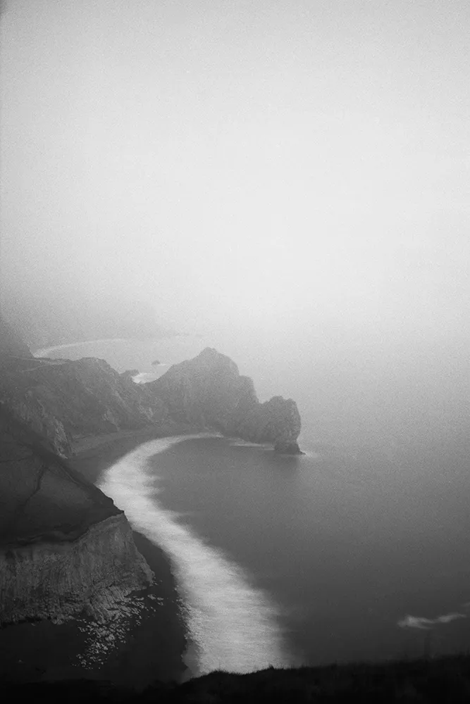 Black and white image of Durdle door from a cliff edge