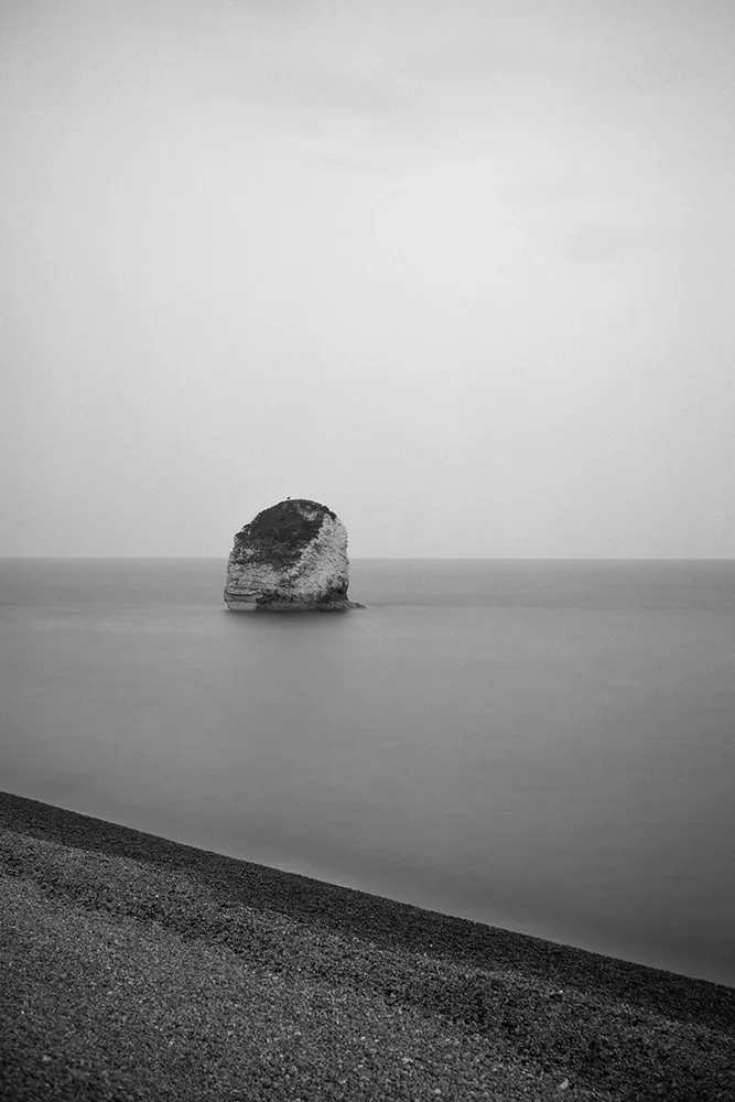 Black and white image of sea stack with the shore in the foreground